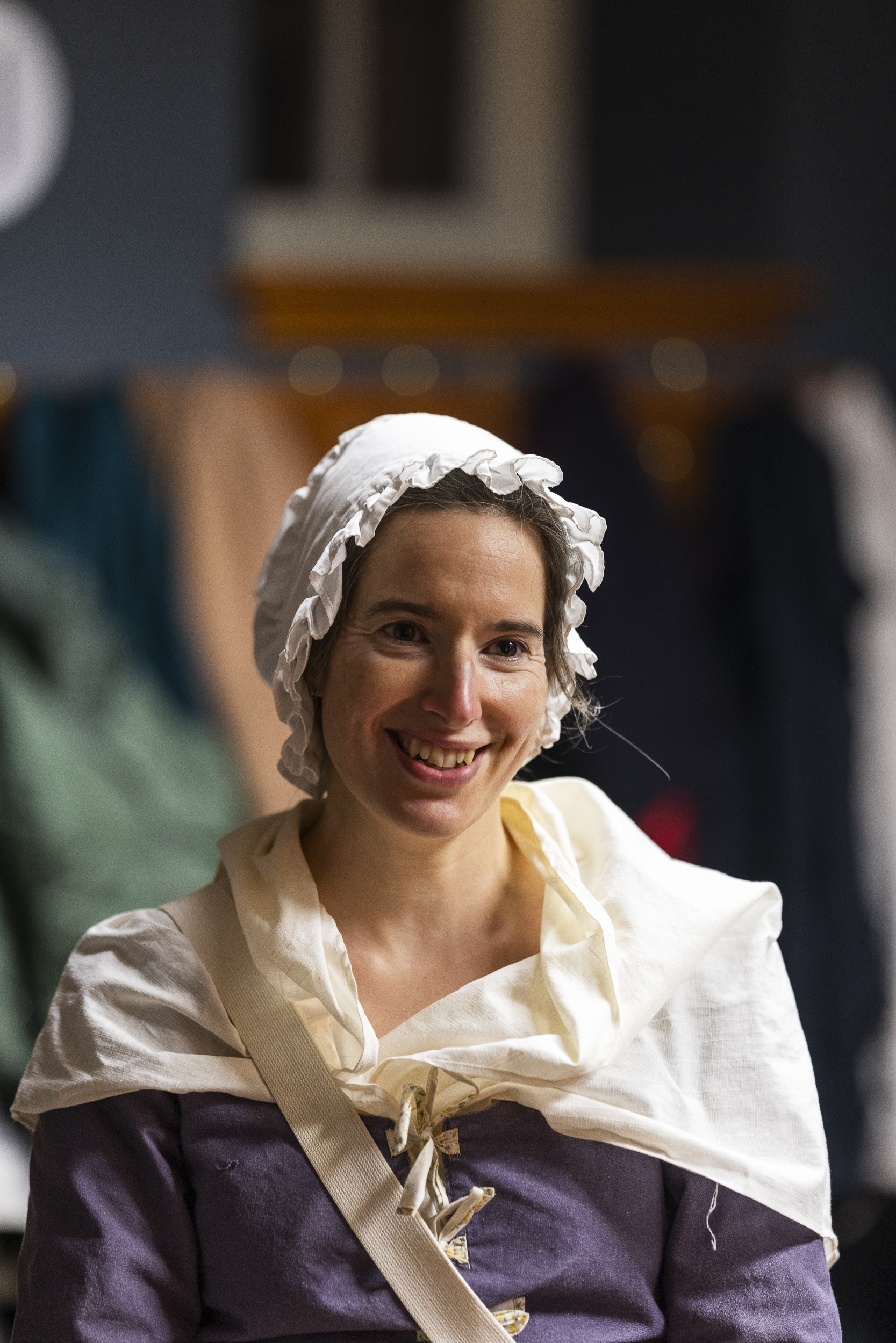 Portrait d'une femme costumée en paysanne portant un bonnet blanc, une robe et un sac sur ses épaules. Portrait of a costumed woman dressed as a peasant, wearing a white bonnet, a dress, and carrying a bag over her shoulder.