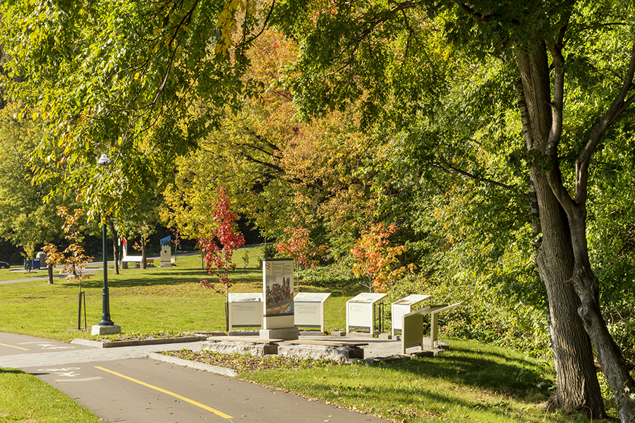 Piste cyclable conduisant vers la côte Gilmour en automne, on aperçoit un panneau d'interprétation. A bike path leading to Gilmour Hill in the fall, with an interpretive sign.