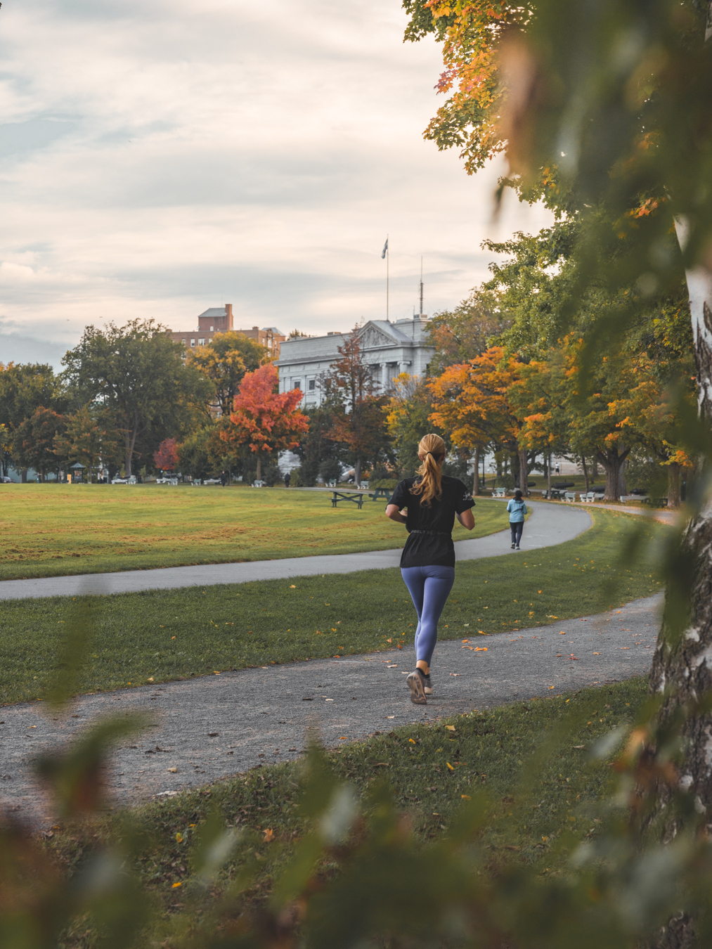 Deux personnes font du jogging sur une piste en automne, entourées d'arbres aux feuilles colorées.