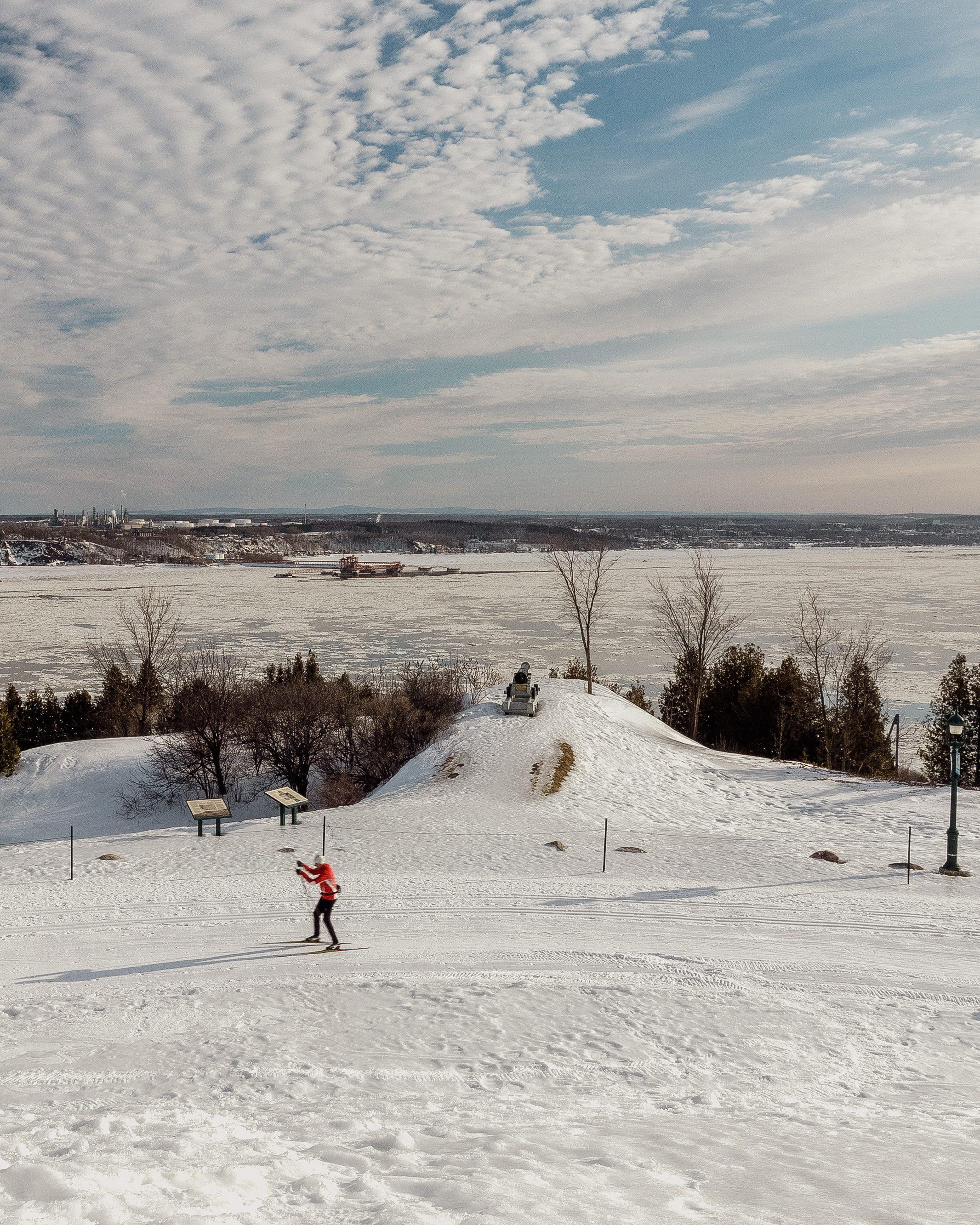 Plan aérien d'un skieur de fond sur les plaines d'Abraham, on aperçoit derrière lui le fleuve Saint-Laurent. 

View of a cross-country skier on the Plains of Abraham, with the St. Lawrence River visible behind him