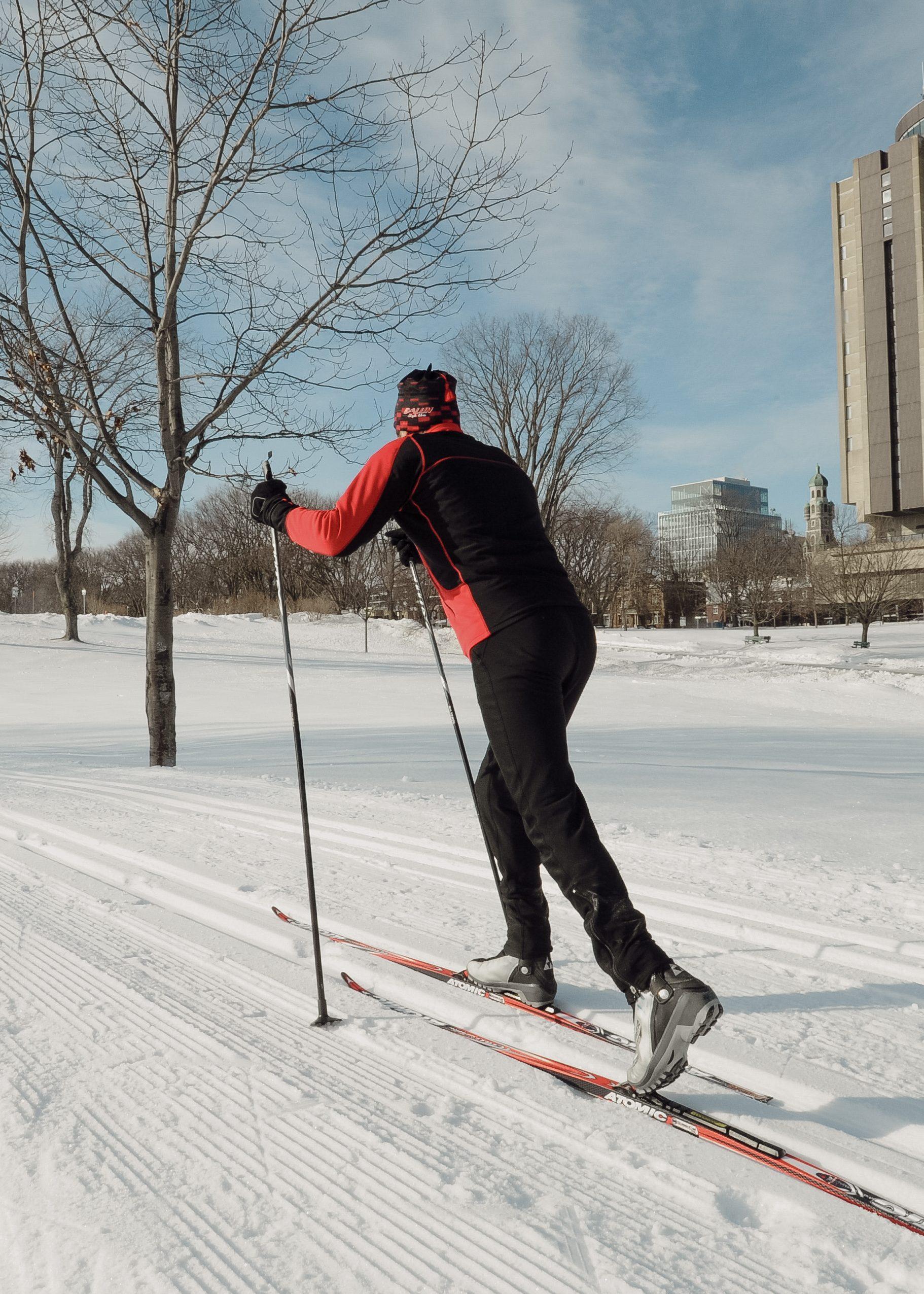 Skieur de fond sur les plaines d'Abraham, de dos, portant des vêtements noir et rouge. Cross-country skier on the Plains of Abraham, seen from behind, wearing black and red clothing.