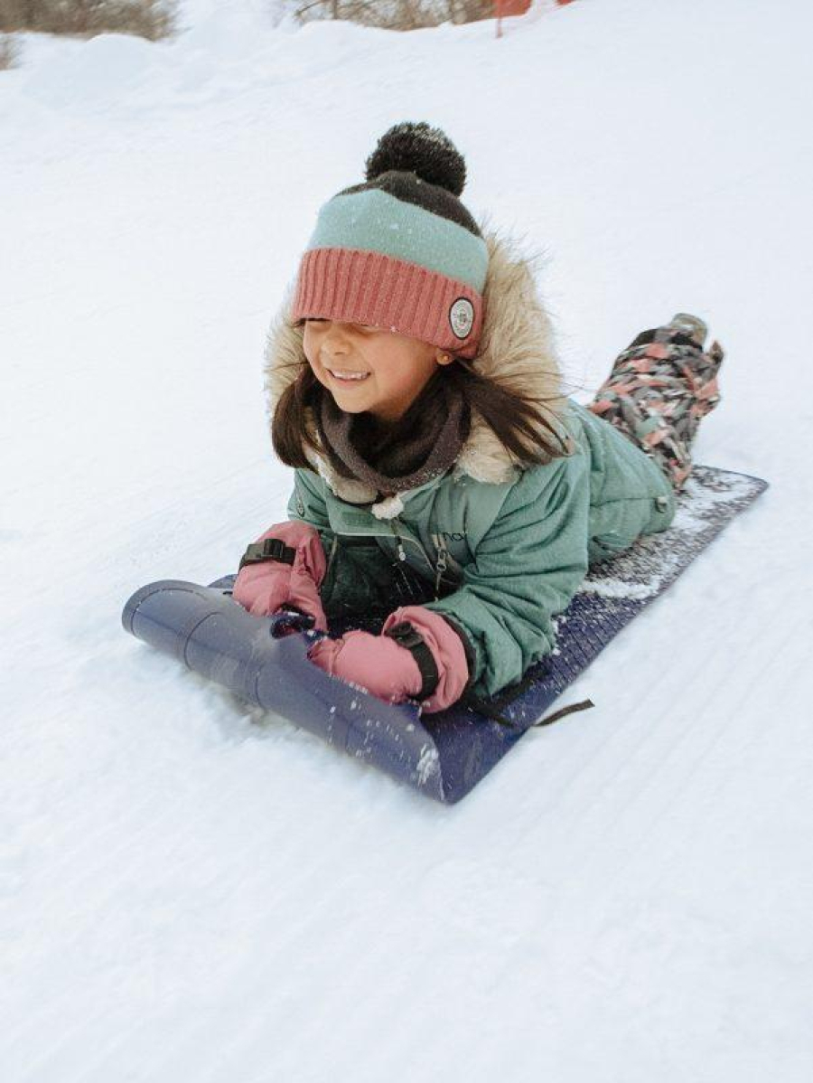 Une fillette glissant sur un tapis à neige sur les plaines d'Abraham, elle porte un habit de neige turquoise et rose. A little girl sliding on a snow carpet on the Plains of Abraham, wearing a turquoise and pink snow suit.