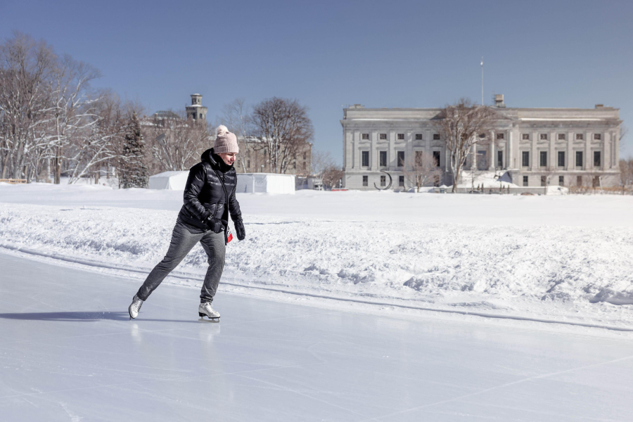 Femme en patin à glace sur l'anneau de glace des plaines d'Abraham, on aperçoit le bâtiment du Musée national des beaux-arts du Québec (MNBAQ) en arrière-plan