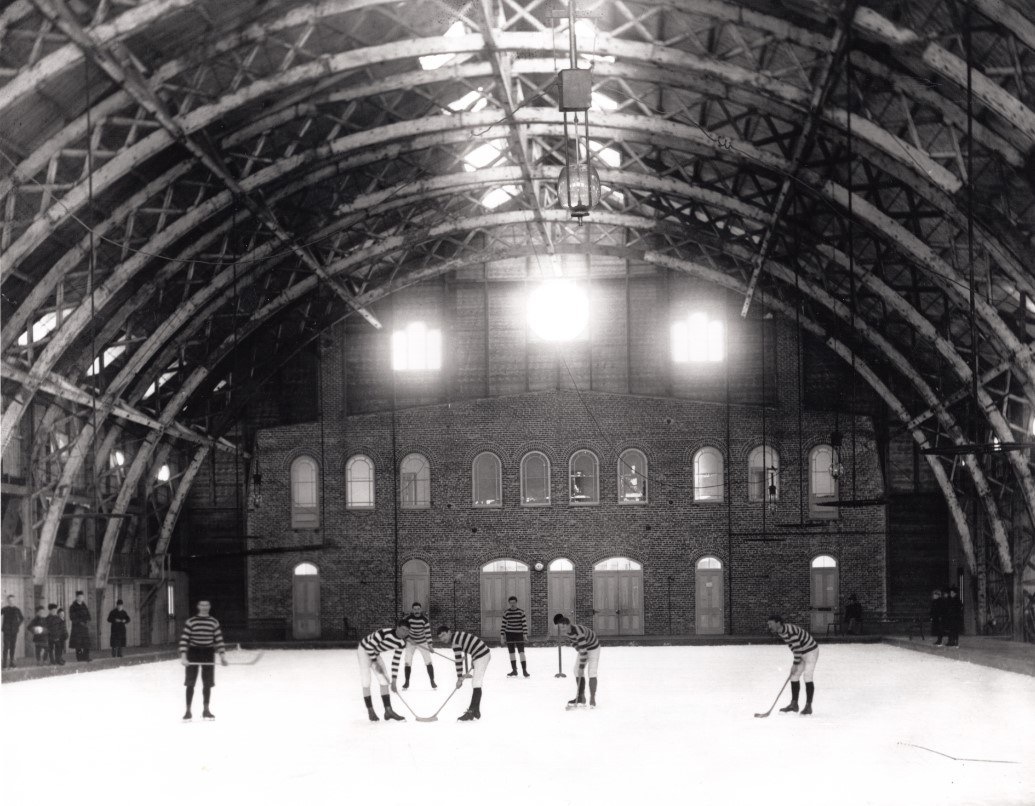 Photo d'archive de l'ancienne patinoire sur les plaines d'Abraham inaugurée en 1892. On aperçoit des joueurs de hockey et un arbitre. Archive photo of the former skating rink on the Plains of Abraham, inaugurated in 1892. The image shows hockey players and a referee.