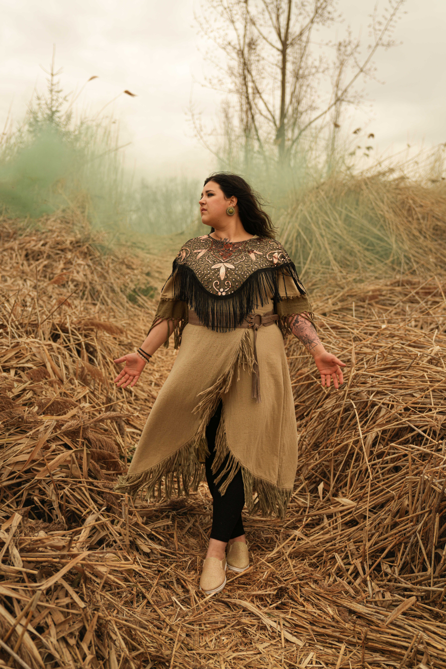 Artiste autochtone Eadsé posant dans un champ avec une fumée verte en arrière-plan