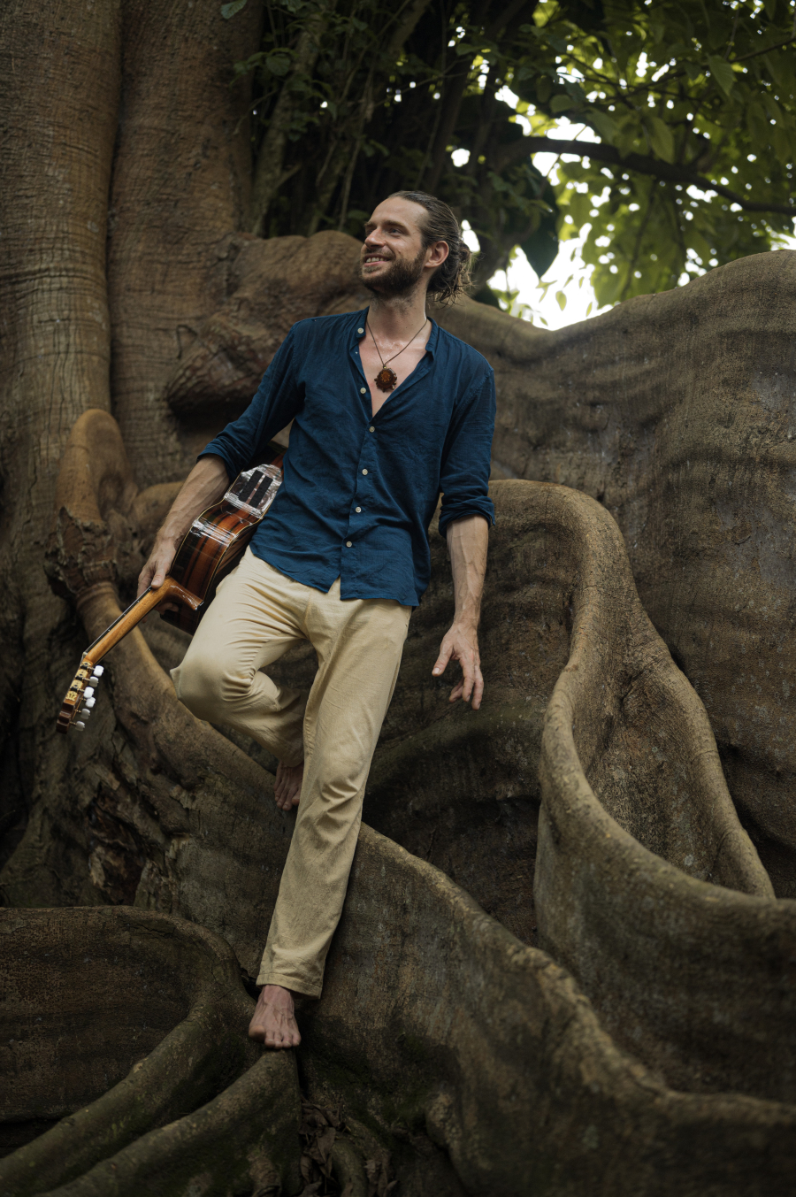 Raph Delaé artiste posant en nature devant un arbre imposant, guitare à la main