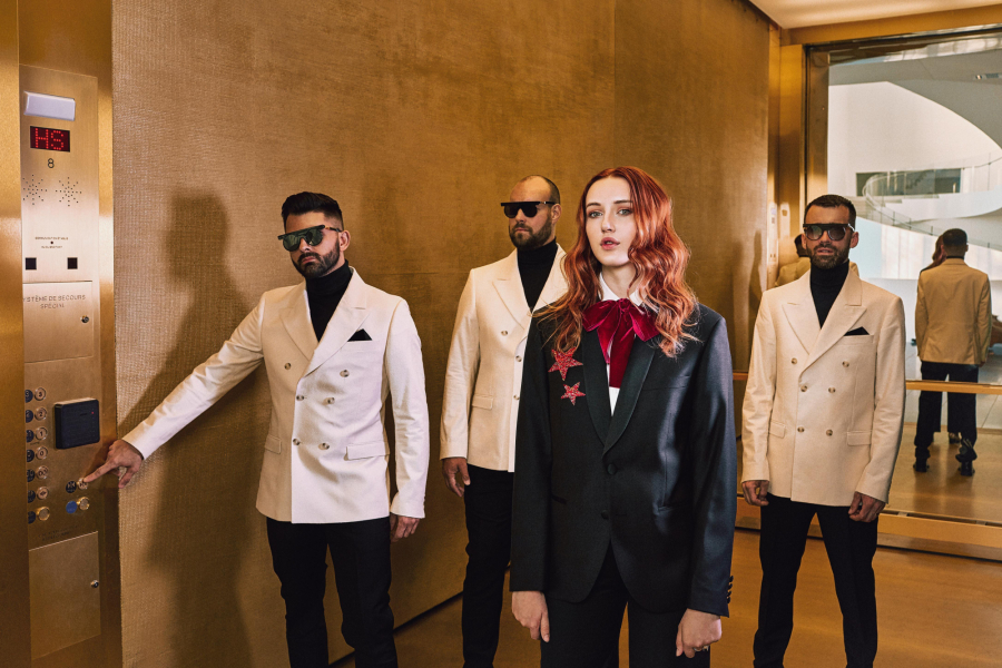 The Lost Finfers, groupe de 4 artistes posant en veston, les hommes portent des lunettes de soleil, la chanteuse porte un veston noir et arbore des cheveux roux