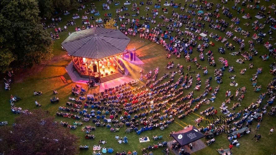 Vue aérienne du kiosque Edwin-Bélanger avec effet de lumière rose et mauve devant une foule assise autour sous forme d'agora naturel sur les plaines d'Abraham