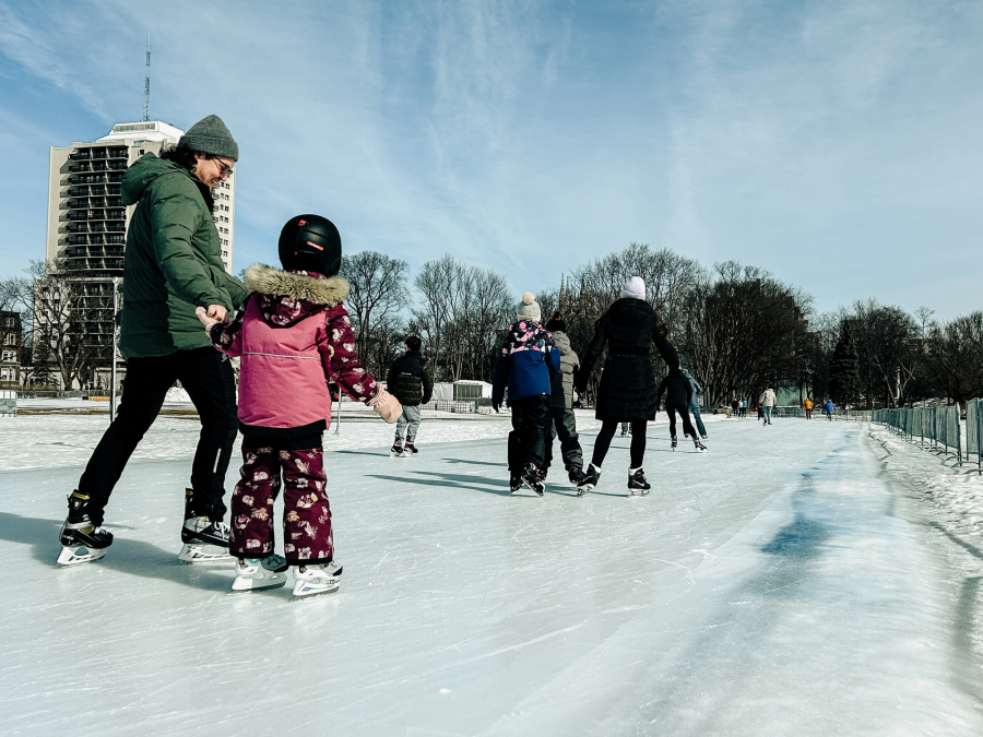Un père et sa fille patinant sur l'anneau de glace des plaines d'Abraham, le père porte un manteau vert et sa fille un manteau rose.