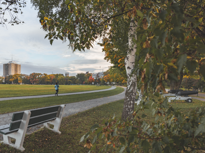 Banc de parc avec une personne qui fait du jogging en automne, des canons sont visibles à l'arrière-plan.