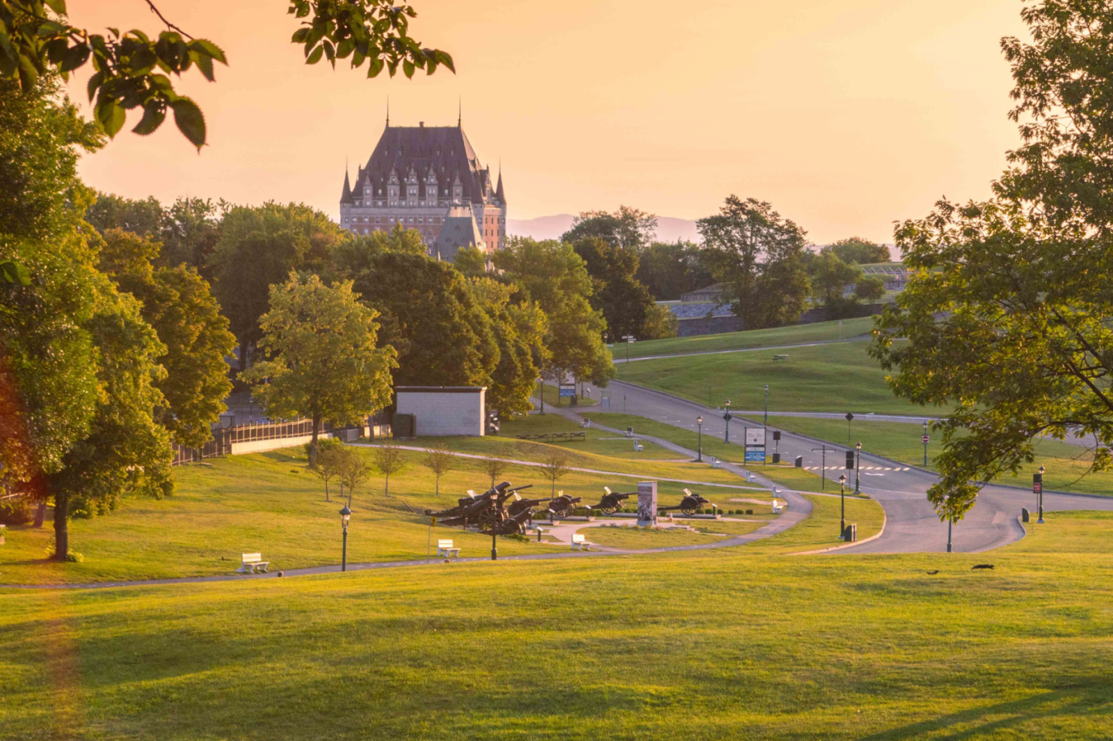 Image des plaines d'Abraham en été au coucher du soleil avec vue sur une partie du Château Frontenac. Image of the Plains of Abraham in summer at sunset, with a view of part of the Château Frontenac.