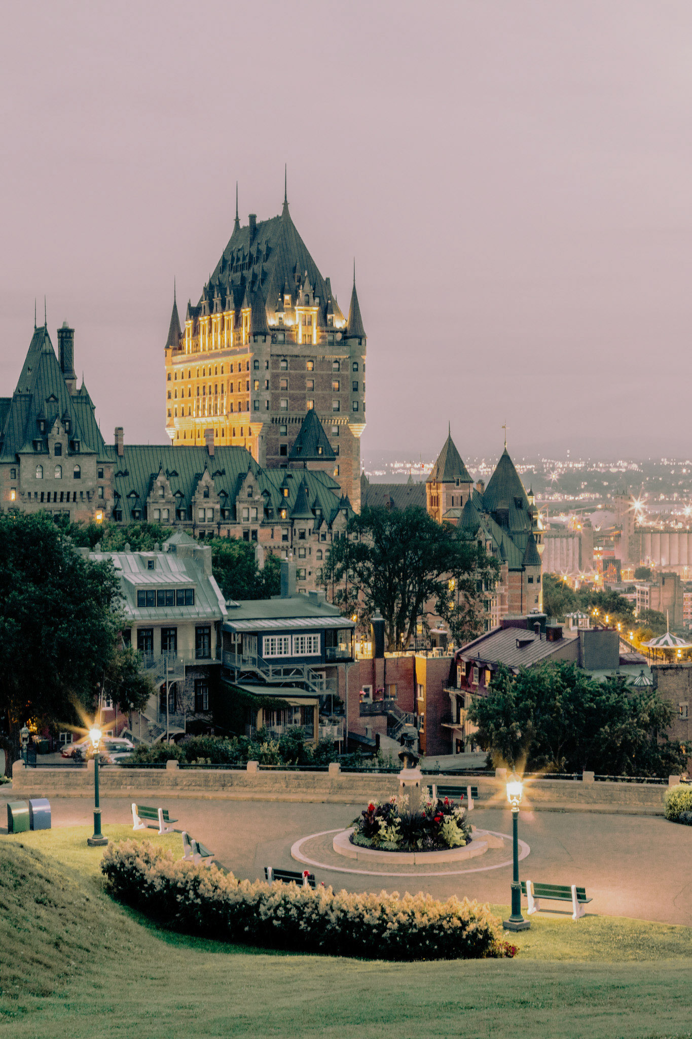 Terrasse Pierre-Dugua-de-Mons en soirée, végétation et maison du Vieux-Québec, vue sur le Château Frontenac de Québec. Pierre-Dugua-de-Mons Terrace in the evening, with vegetation and a house from Old Quebec, view of the Château Frontenac of Québec City.