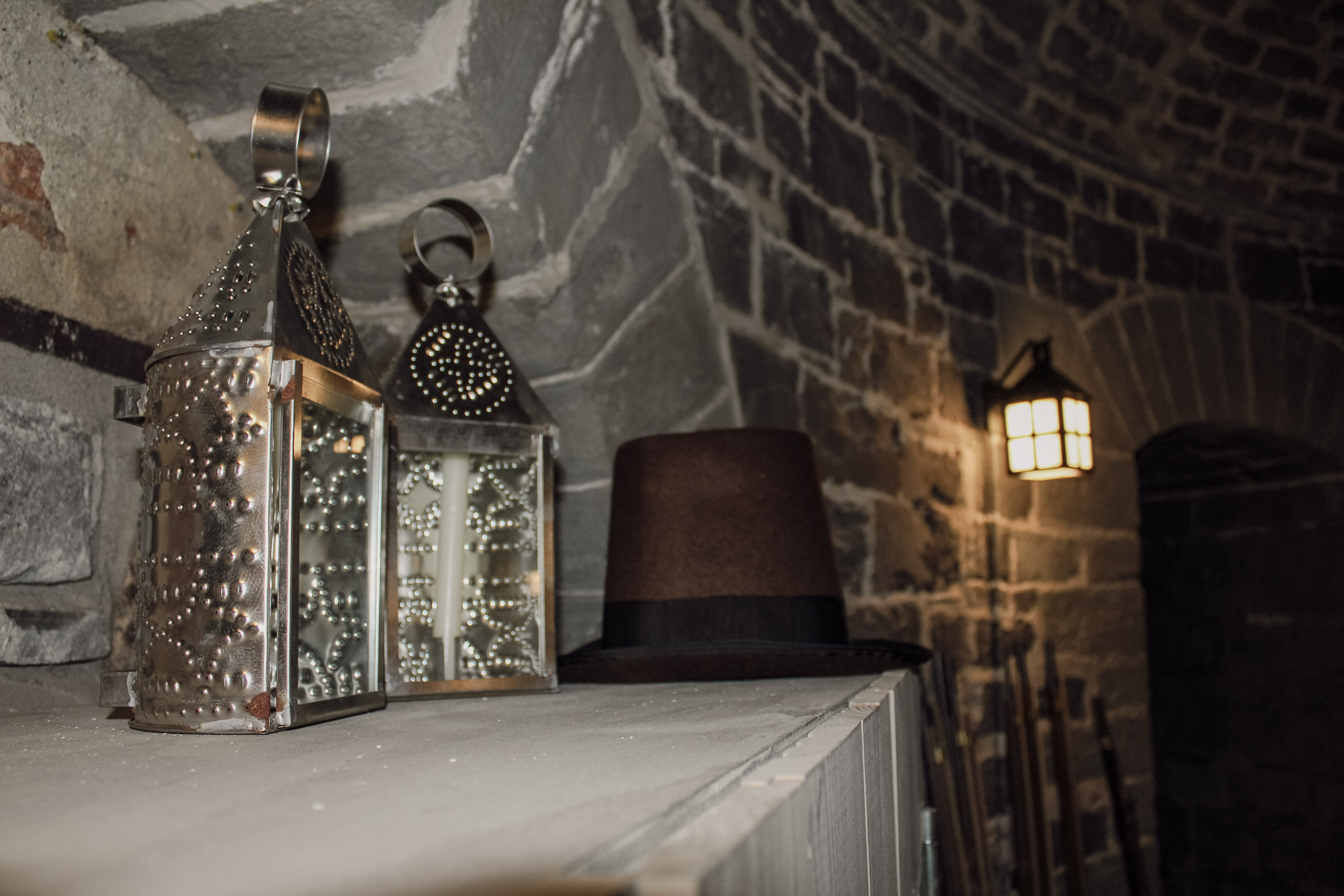 Lanternes en argent et un chapeau brun sur un meuble blanc posé devant un mur de pierres de la tour Martello 4. Silver lanterns and a brown hat on a white piece of furniture placed in front of a stone wall of Martello Tower 4.