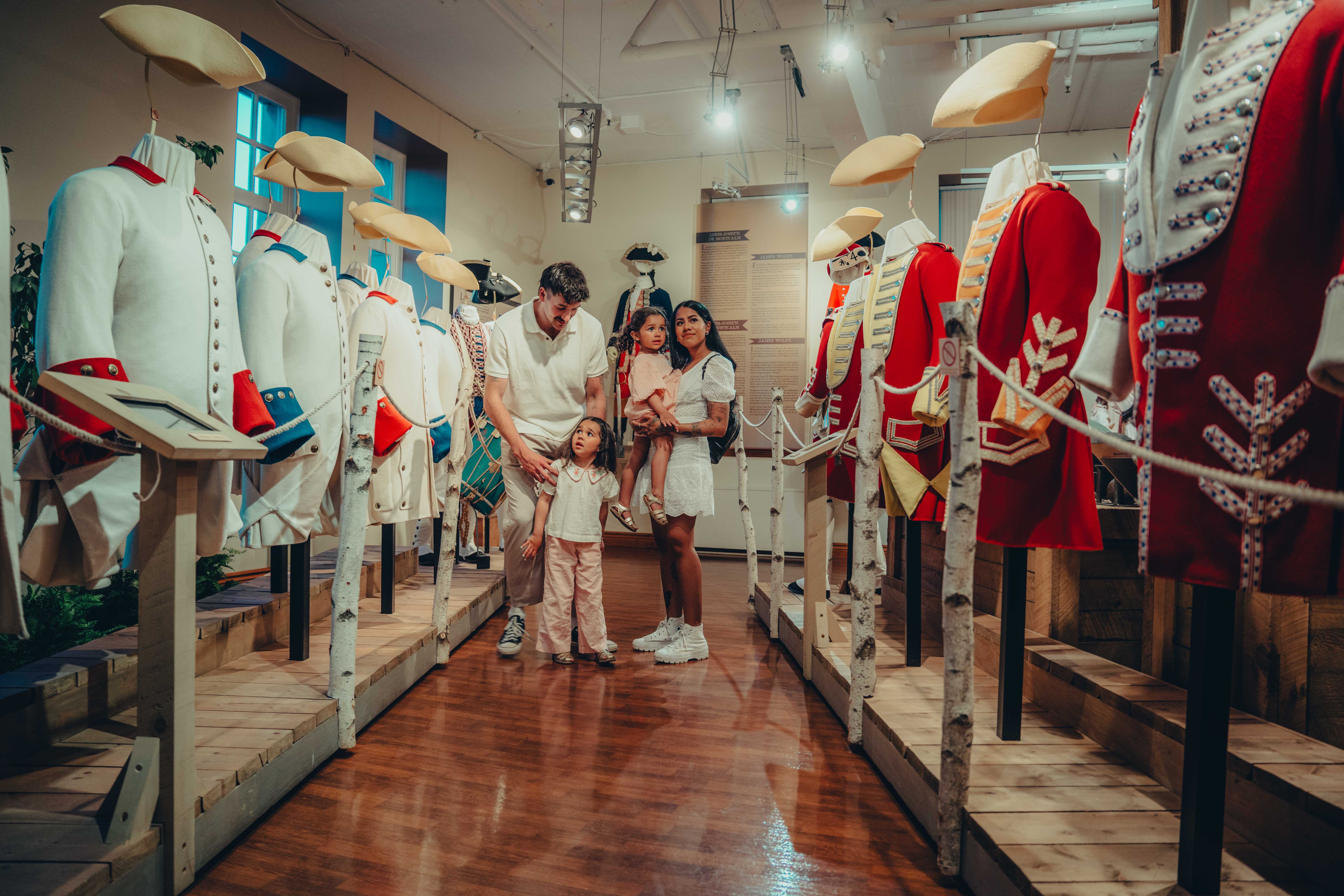 Les parents et leurs deux fillettes contemplent des uniformes en exposition. The parents and their two young daughters are admiring uniforms on display.