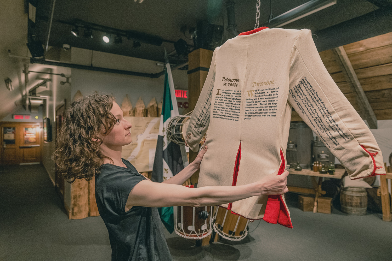 Une femme tenant entre ses mains un uniforme contenant des textes et soutenu dans les airs par une chaine. A woman holding a uniform with text on it, suspended in the air by a chain.