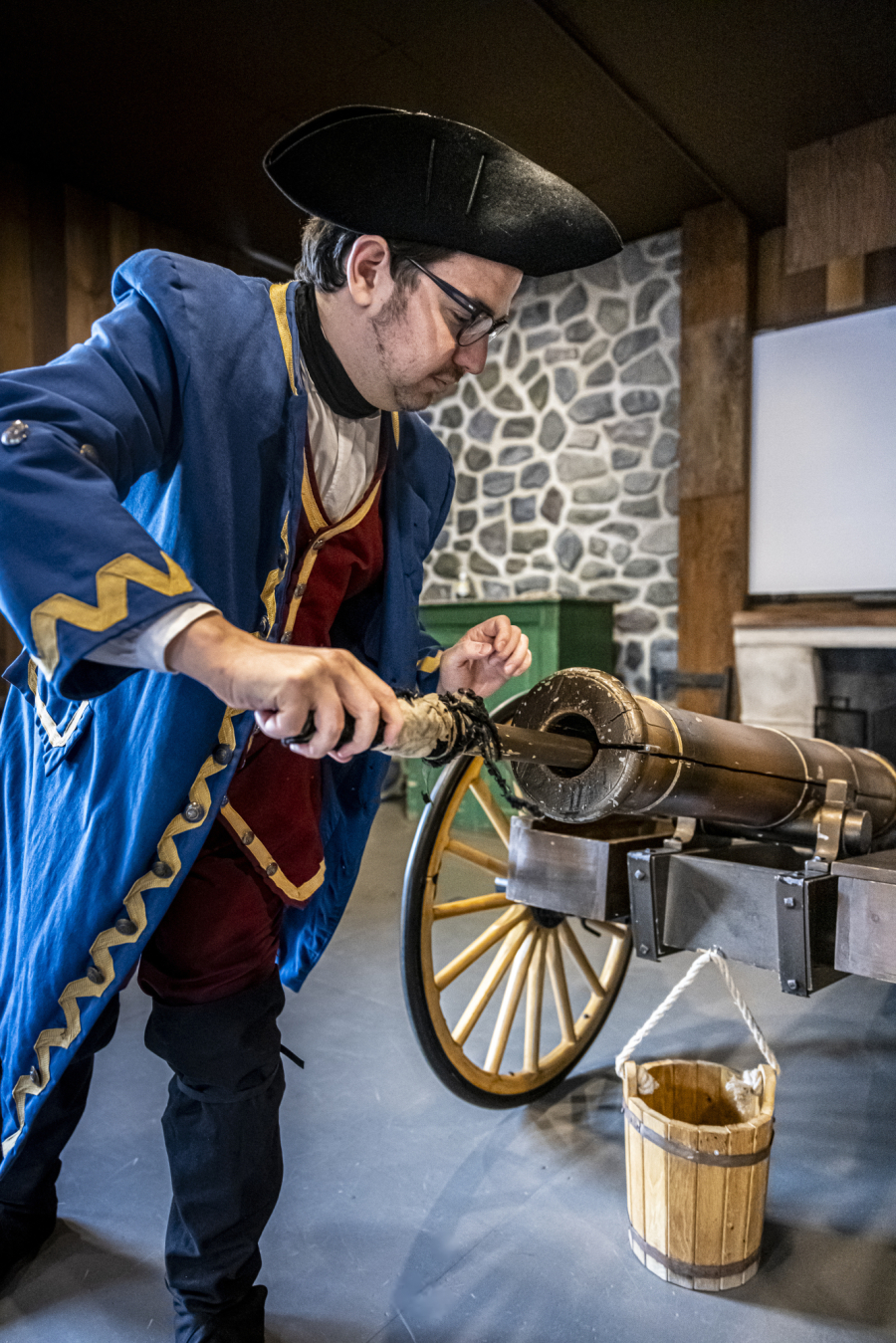 Photo d'un employé du Musée des plaines d'Abraham portant un costume d'époque, on aperçoit un canon dans une salle du Musée. Photo of a Plains of Abraham Museum employee dressed in period costume, with a cannon visible in a museum room.